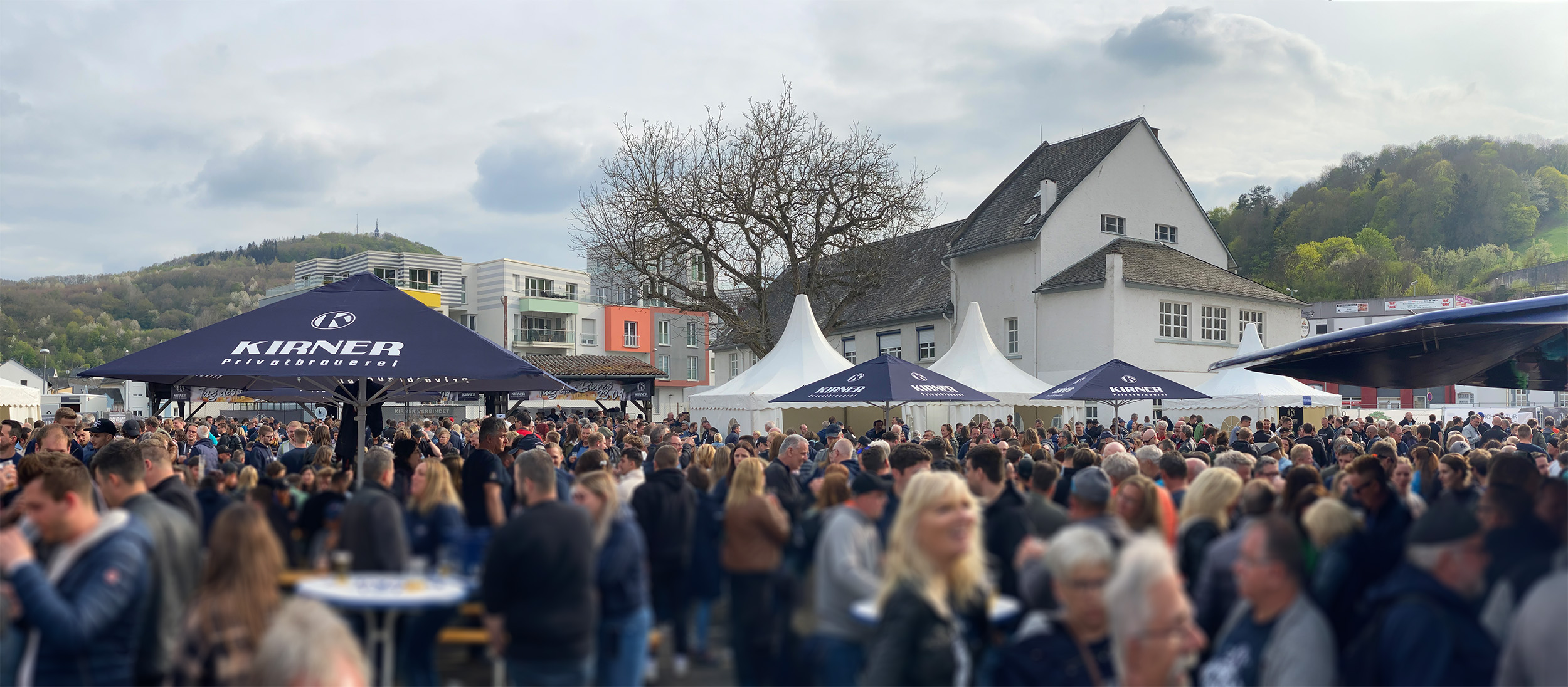 Panoramafoto vom Hoffest bei der Kirner Brauerei mit vielen Menschen und gebrandeten Sonnenschirmen in Blau weiss